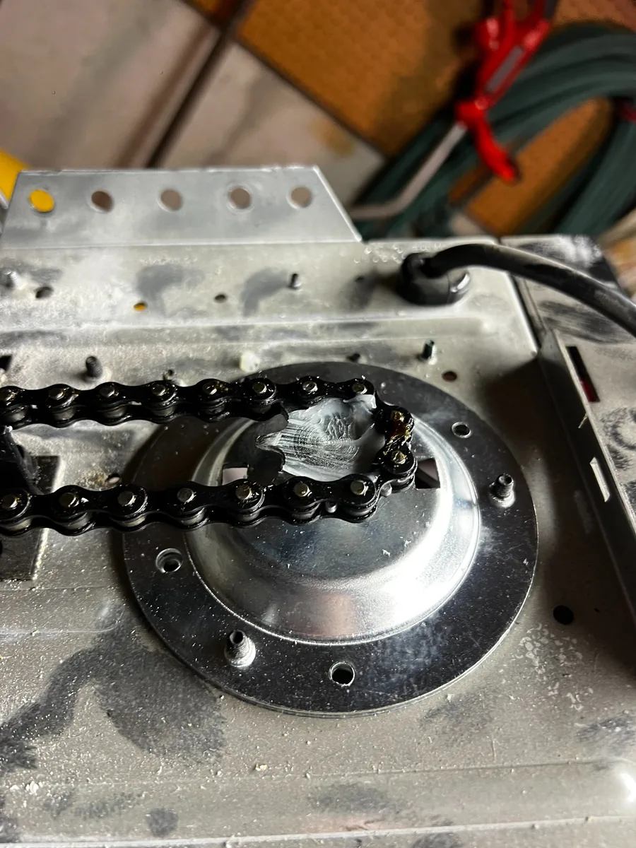 Close-up of a garage door opener chain wrapped around the drive sprocket on top of the motor housing.