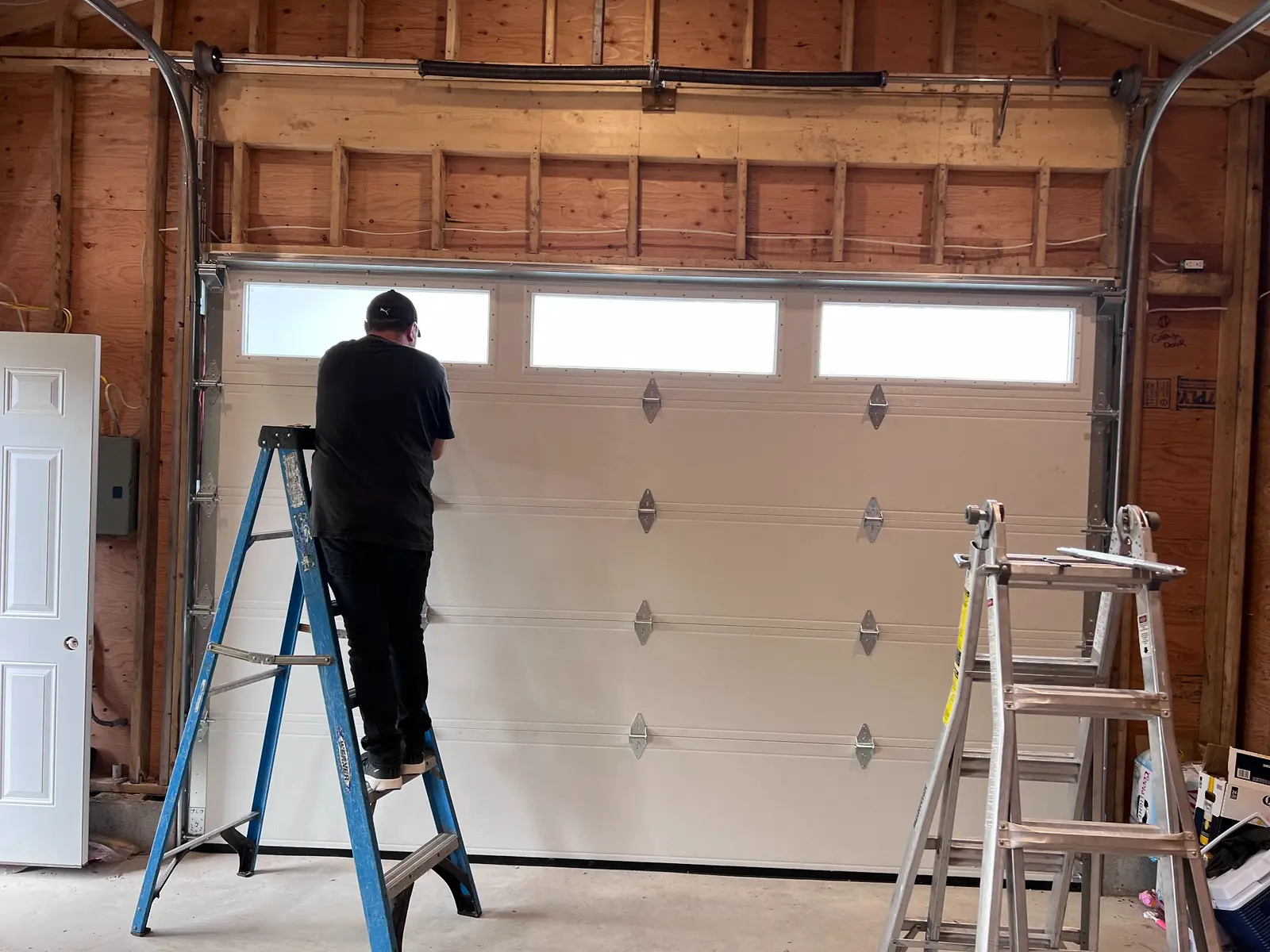 Residential garage door service Technician on a ladder beside a residential garage door with overhead torsion springs