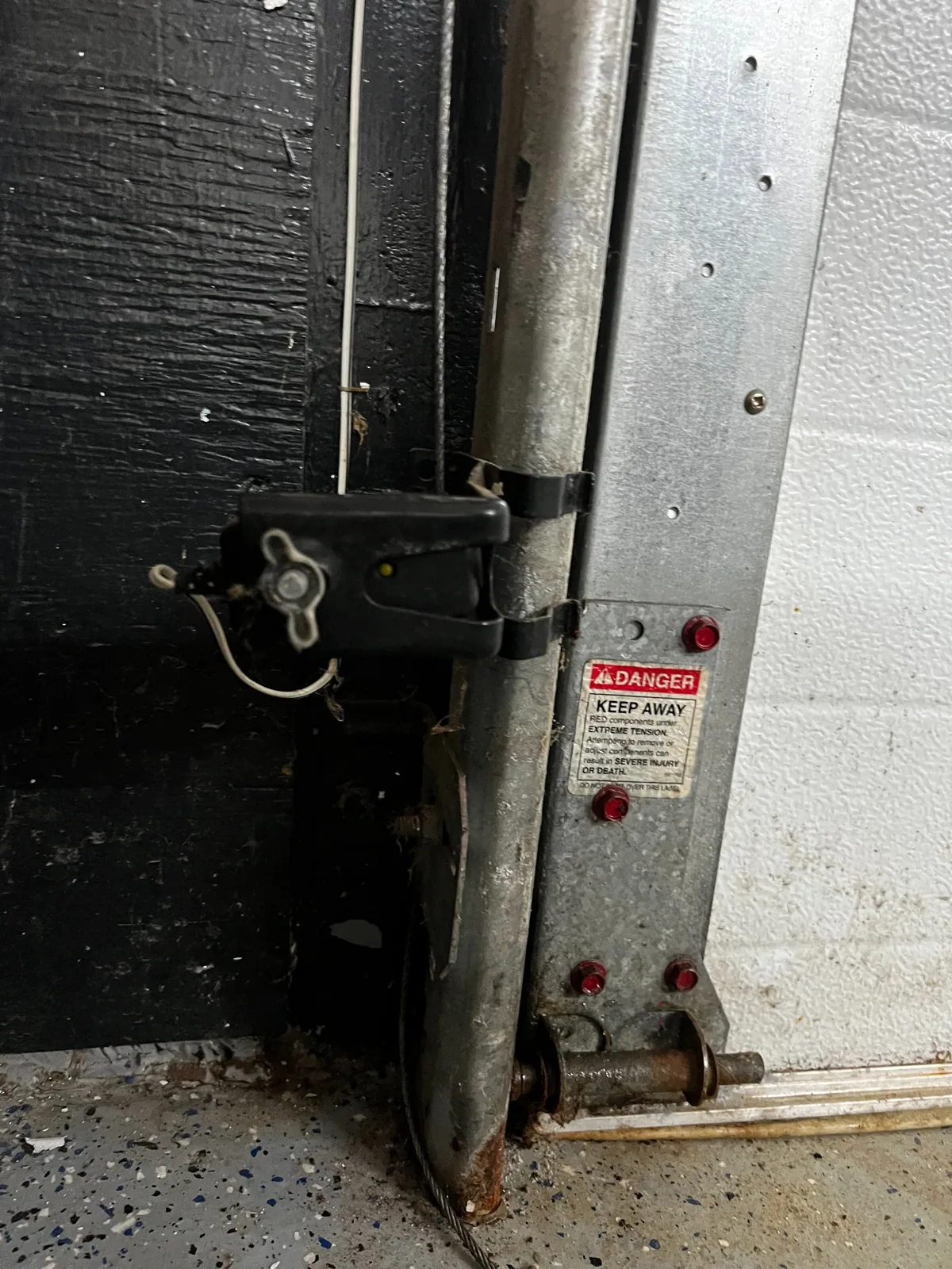 Garage door bottom bracket and cable connection marked as a high-tension component